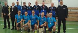 Zdjęcie zawodników zwycięskiej drużyny KP PSP Brzeziny oraz zaproszonych gości i organizatorów. Zawodnicy w strojach sportowych zaś goście w mundurach służbowych PSP.