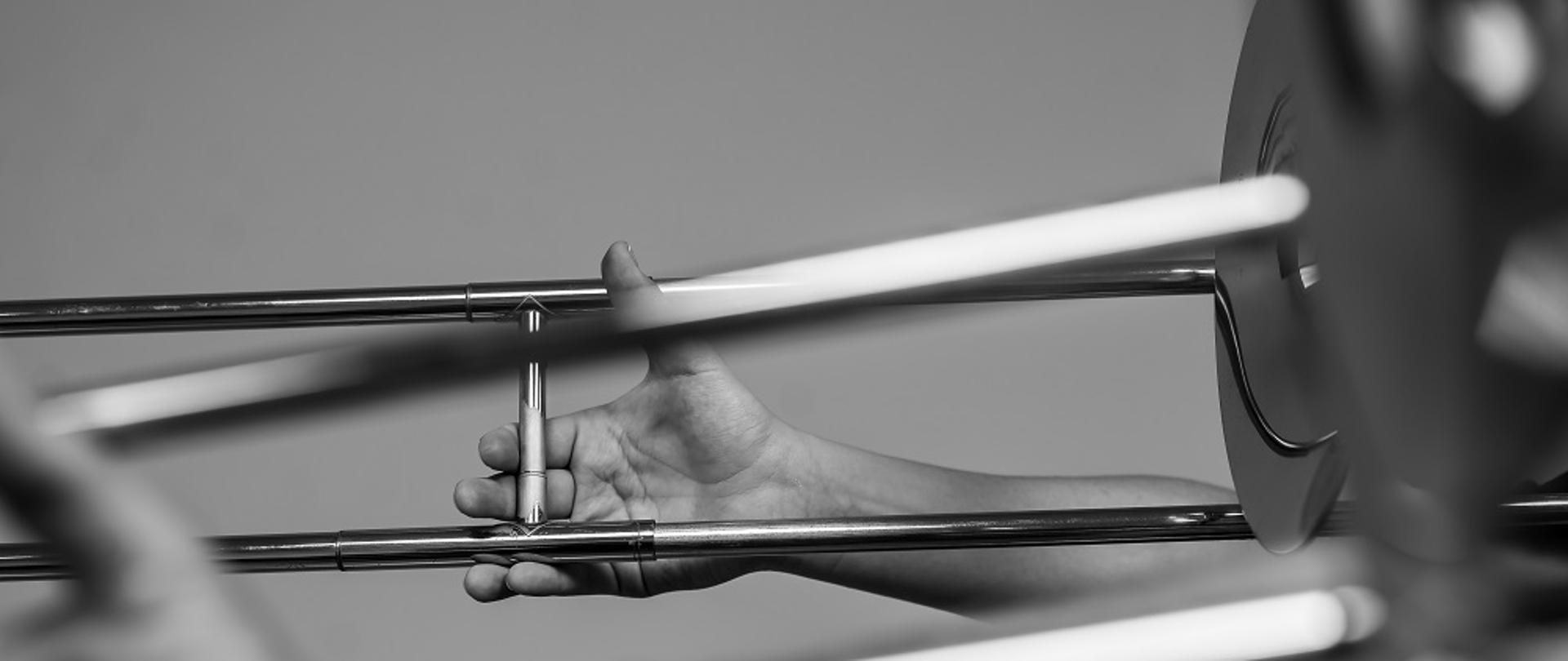 czarno-białe zdjęcie przedstawia detal puzonu, zbliżenie na rękę trzymającą suwak