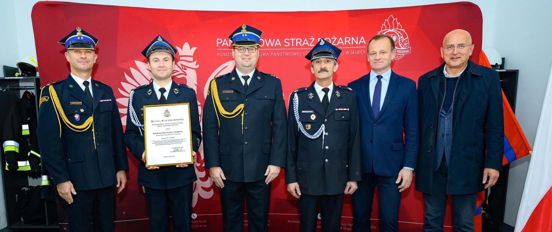 Strażacy oraz osoby cywilne na tle ścianki PSP