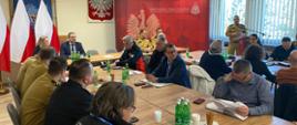 na zdjęciu sala sztabowa w trakcie spotkania roboczego, w tle godło i flaga Polski