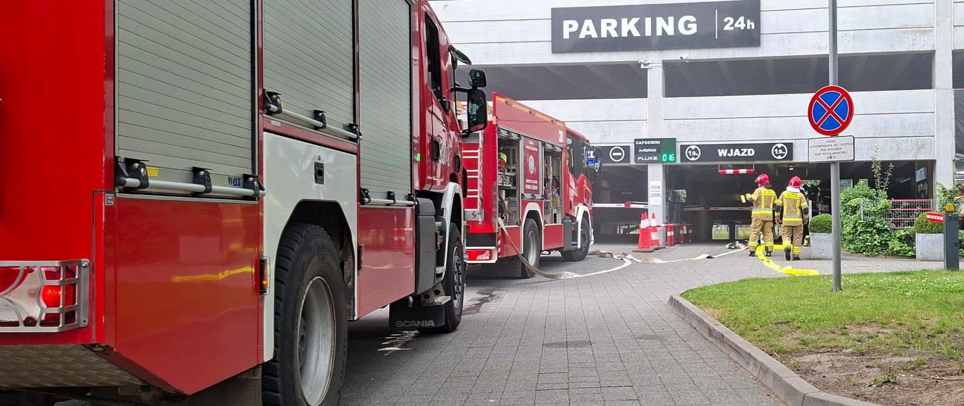 Wozy strażackie i strażacy prowadzą działania ratowniczo-gaśnicze przy wjeździe do parkingu wielopoziomowego