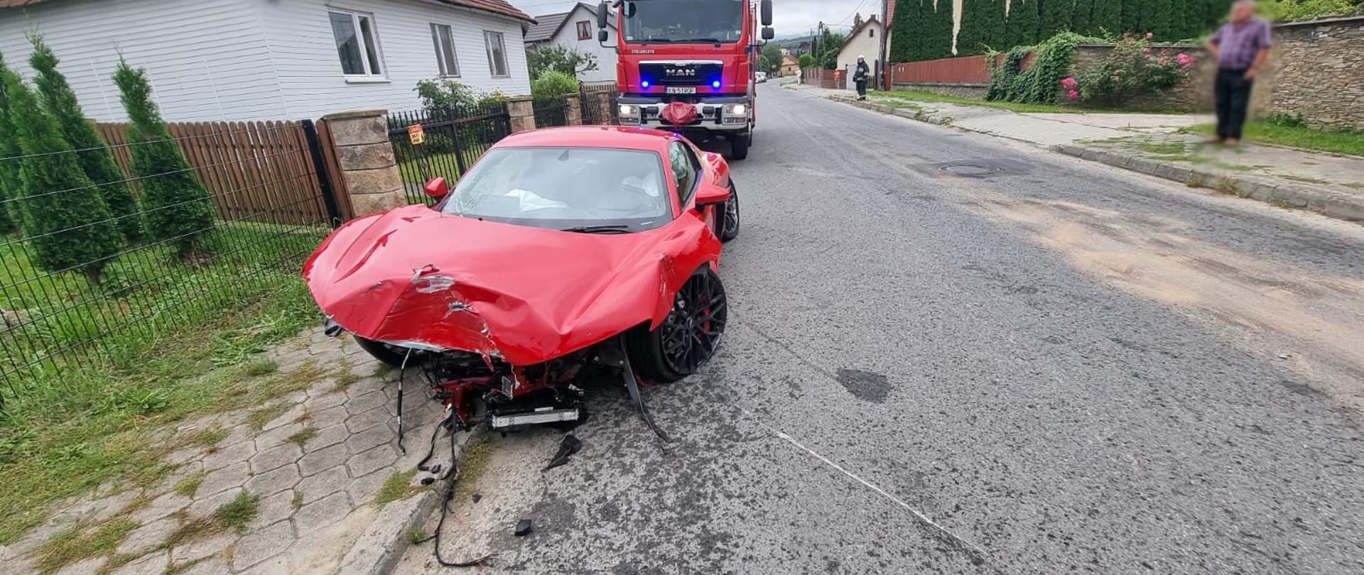 Rozbity samochód osobowy na poboczu za nim samochód pożarniczy.