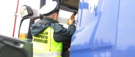 Inspektor lubuskiej Inspekcji Transportu Drogowego stoi w wejściu do kabiny ciężarówki, trzyma w ręku alkomat przesiewowy i czeka na wynik badania trzeźwości kierowcy.