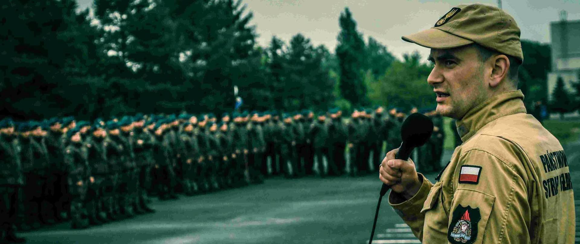 Funkcjonariusz PSP przemawia do uczestników ustawionych w szeregu podczas zbiórki związanej z ćwiczenia kryzysowymi
