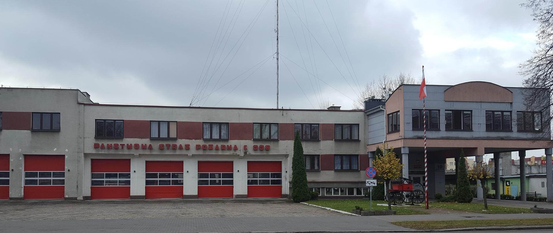 Na zdjęciu widać budynek komendy powiatowej państwowej straży pożarnej w Iławie od strony ulicy Wyszyńskiego. Od lewej strony kolejno sześć czerwonych bram wjazdowych do garaży. Bramy posiadają w środkowej części pas przeszklenia na całej szerokości. Dalej po prawej stronie widać dwa okna. Nad garażami na poziomie pierwszego piętra widać osiem okien. Między oknami ciągnie się czerwony pas elewacji. Pomiędzy oknami a bramami garażowymi widać napis „Państwowa Straż Pożarna” dalej słuchawkę telefonu i cyfry 998. Po prawej stronie widać wzniesioną na słupach dalszą część budynku komendy, która połączona jest z pozostałą częścią strażnicy i dodatkowo wysunięta kilka metrów przed nią. Przed bramami wjazdowymi widoczny plac manewrowy. Po prawej stronie przed budynkiem widać trawnik. W tej części przed budynkiem znajduje się maszt flagowy z podniesioną biało-czerwoną flagą. Za masztem na niskim białym postumencie widoczna zabytkowa pompa pożarnicza.