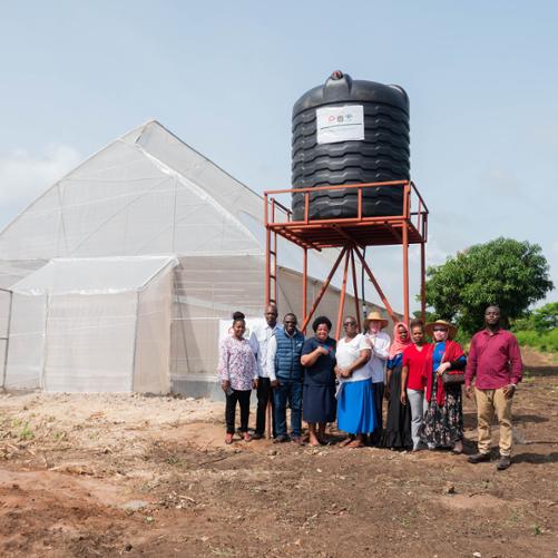 Grupa osób pozuje do zdjęcia przed zbiornikiem na wodę i szklarnią 