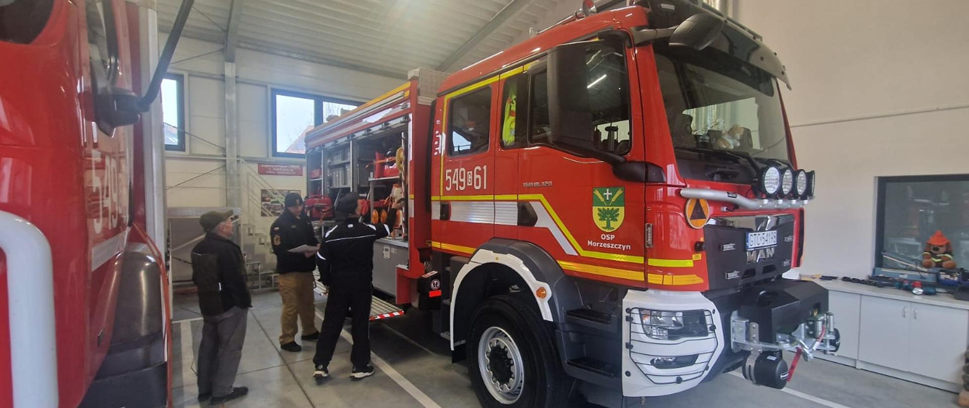 Na garażu trzy osoby przy samochodzie strażackim podczas kontroli