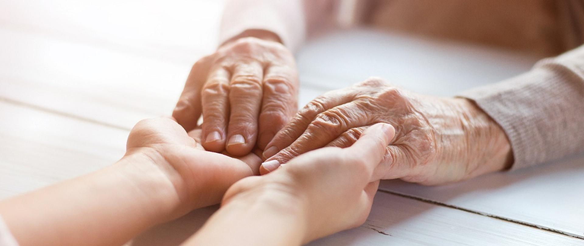 Dłonie młodej osoby trzymające dłonie starszego mężczyzny