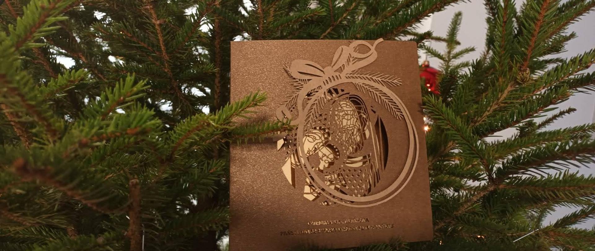 Kartka świąteczna umieszczona na choince przybranej bombkami.
