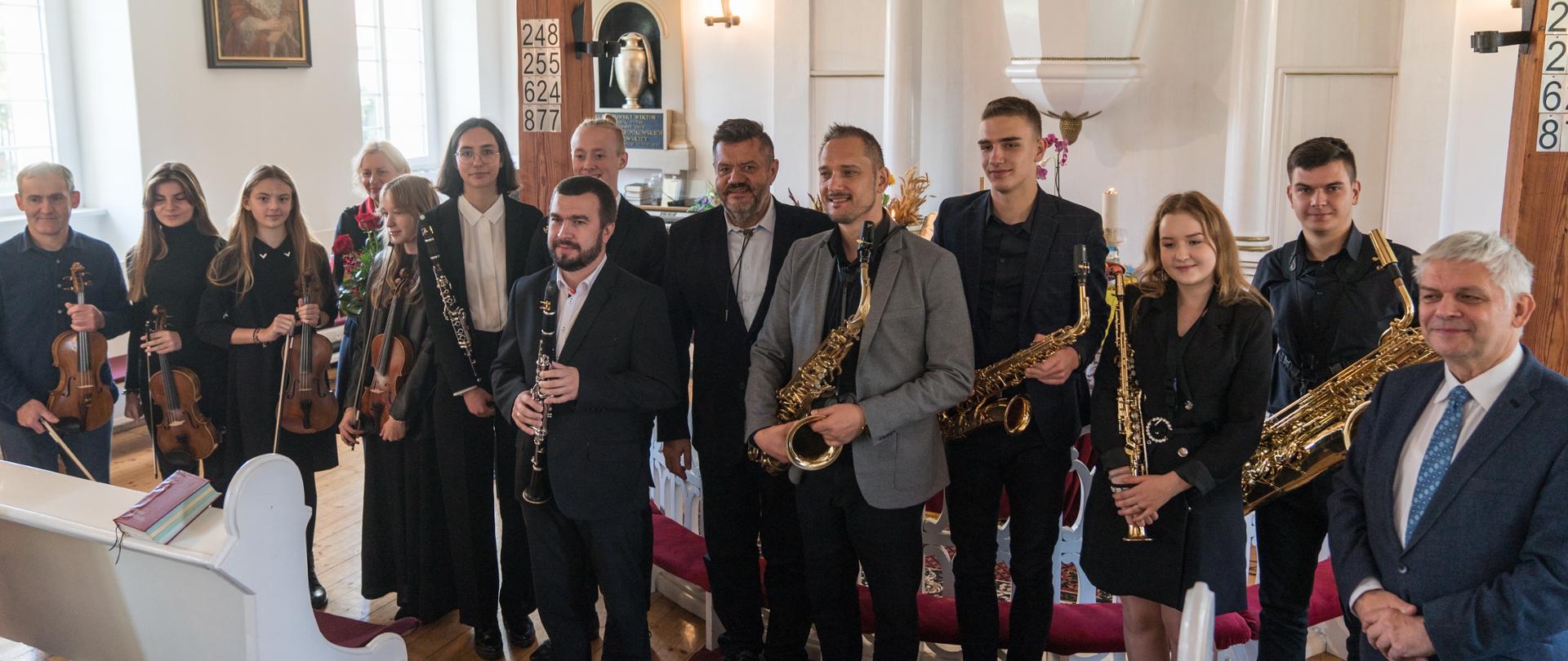 Uczestnicy koncertu w kościele przed ołtarzem trzymają instrumenty
