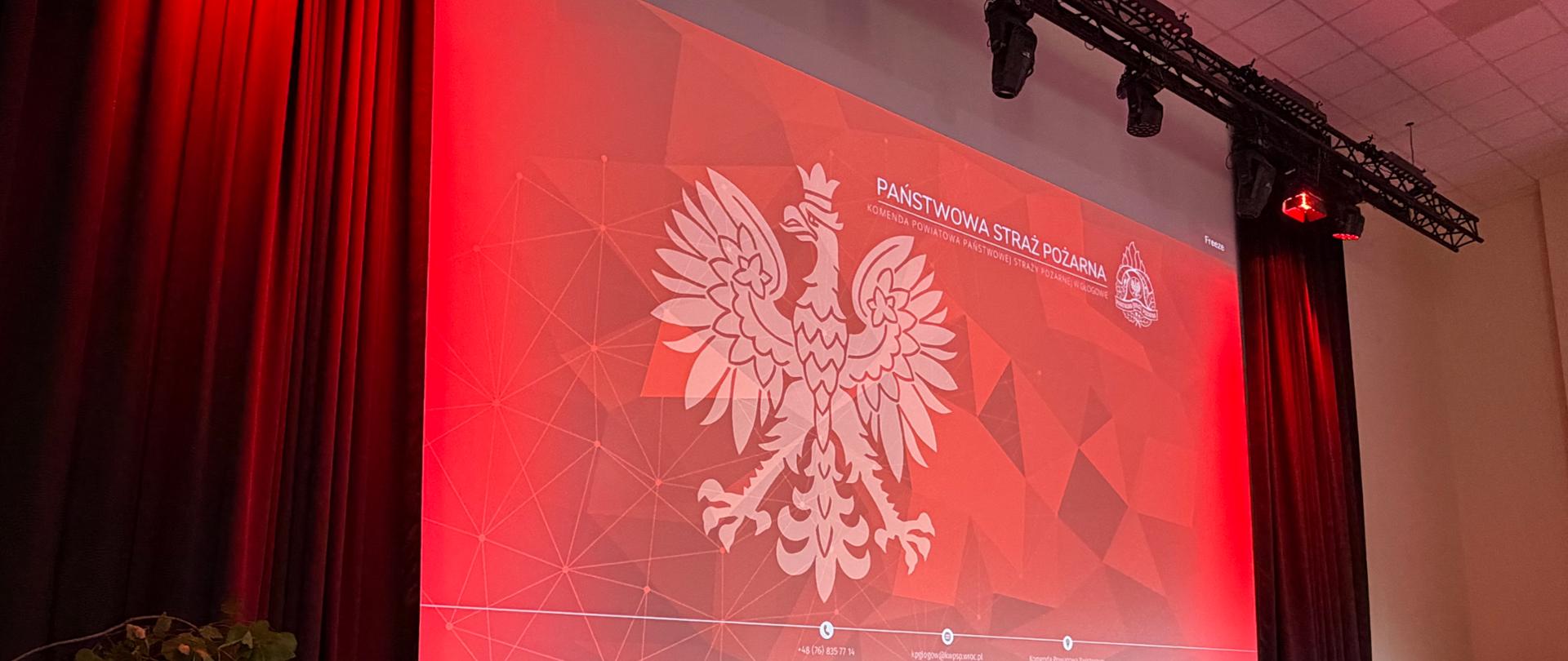 Ekran projekcyjny z grafiką Komendy Powiatowej Państwowej Straży Pożarnej w Głogowie podczas wydarzenia w Miejskim Centrum Integracji „Jubilat”.