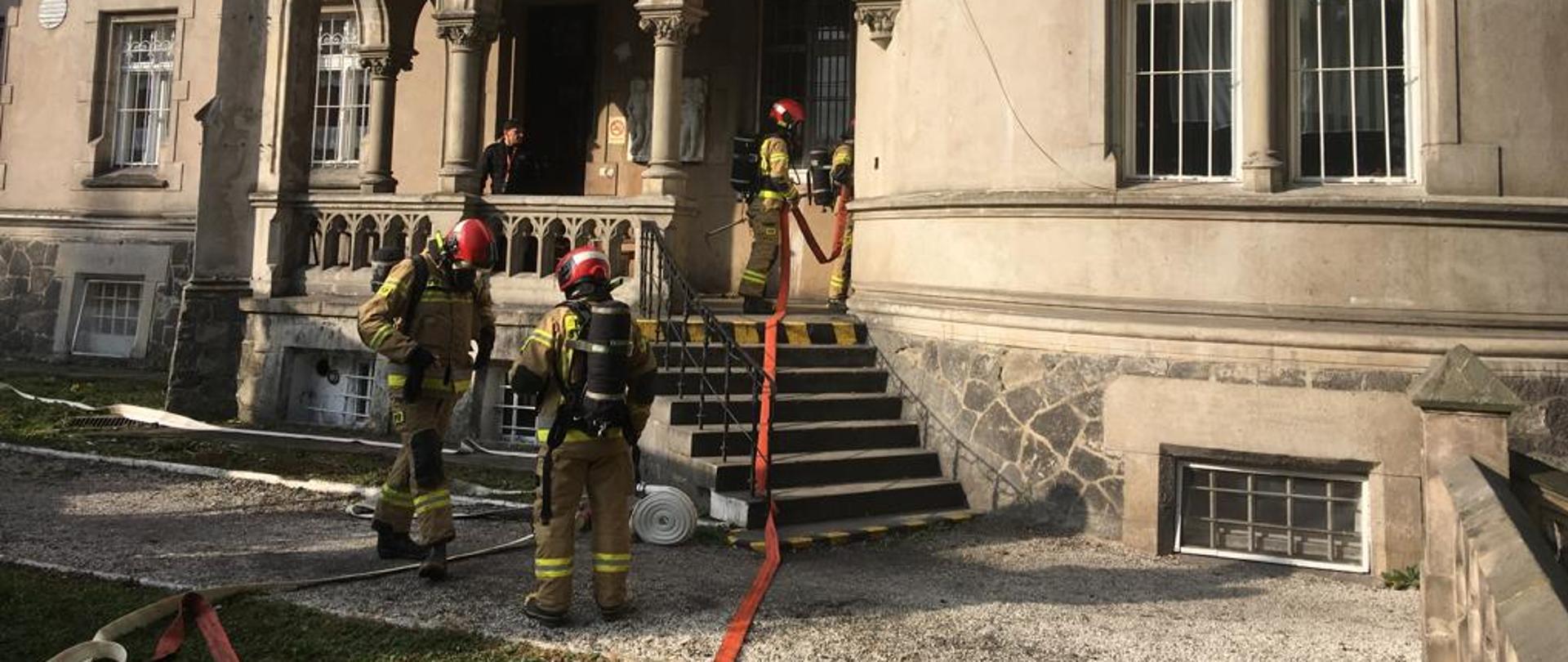 Strażacy z rozwiniętą linią gaśniczą wchodzący do DPS-u.