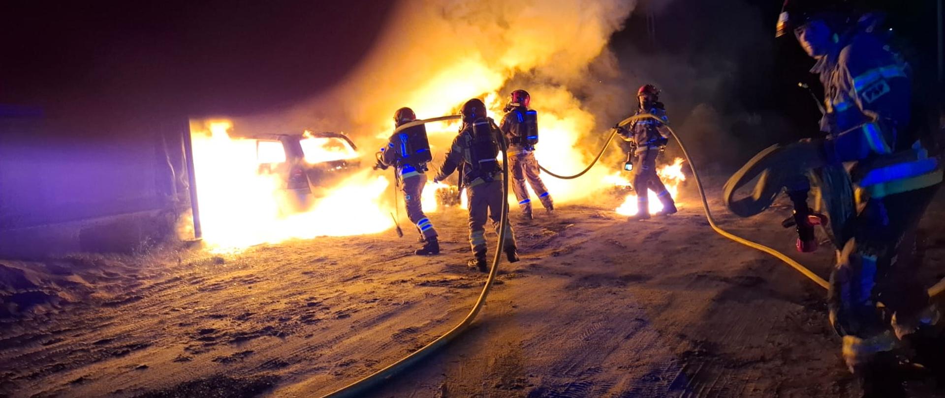 Dwie roty strażaków podają prądy gaśnicze na palące się samochody