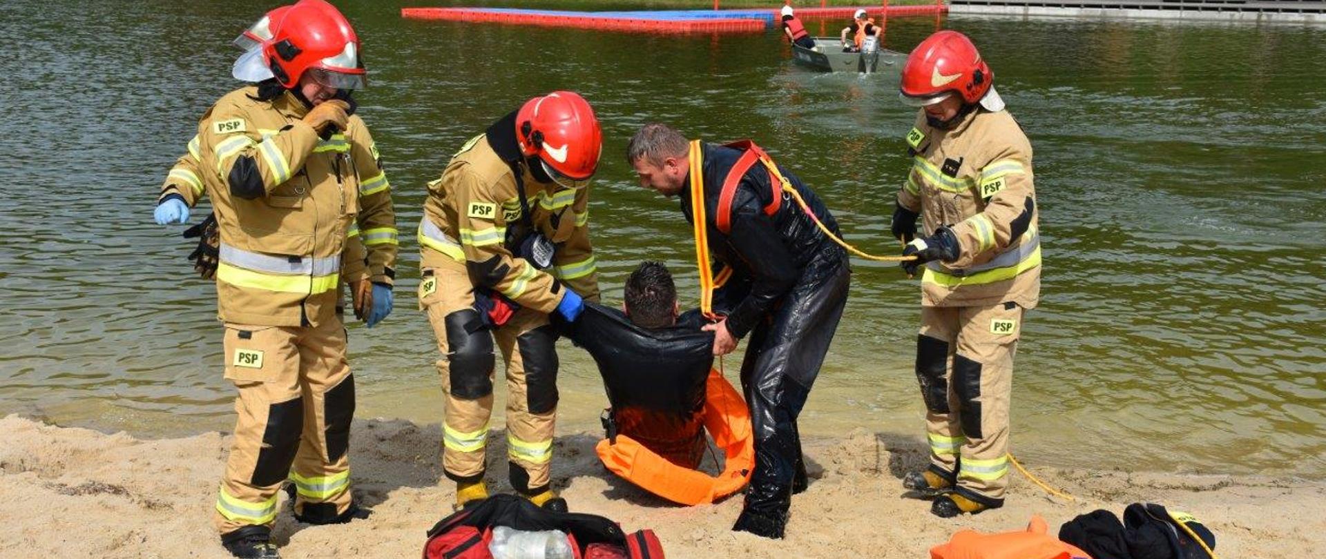 Zdjęcie przedstawia strażaków którzy wyciągnęli za pomocą liny wody pozoranta - będą udzielać mu pomocy medycznej.