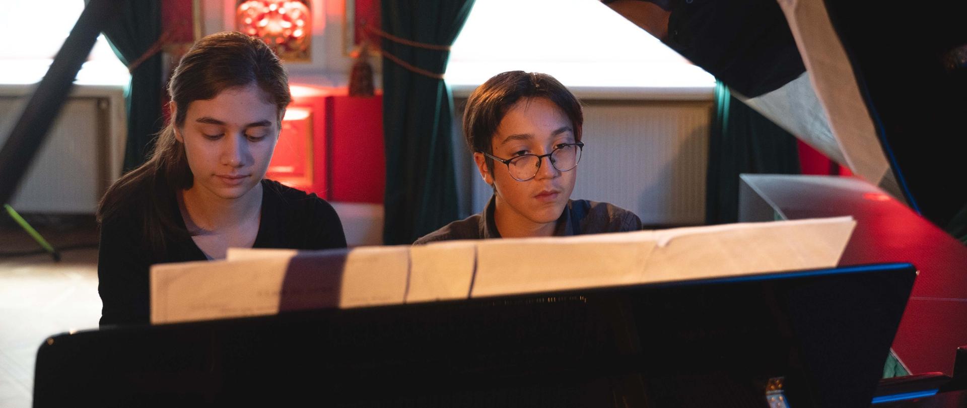 zdjęcie przedstawia dwoje uczniów grających w duecie na fortepianie, ujęcie od przodu pod podniesionym skrzydłem fortepianu