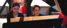 zdjęcie przedstawia dwoje uczniów grających w duecie na fortepianie, ujęcie od przodu pod podniesionym skrzydłem fortepianu