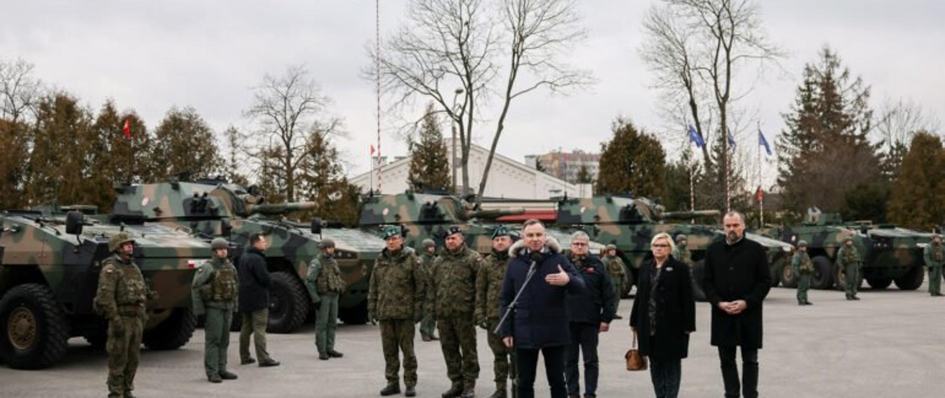 Prezydent RP Andrzej Duda przemawia w Rzeszowie. Za prezydentem stoi grypa żołnierzy na tle czołgów. 