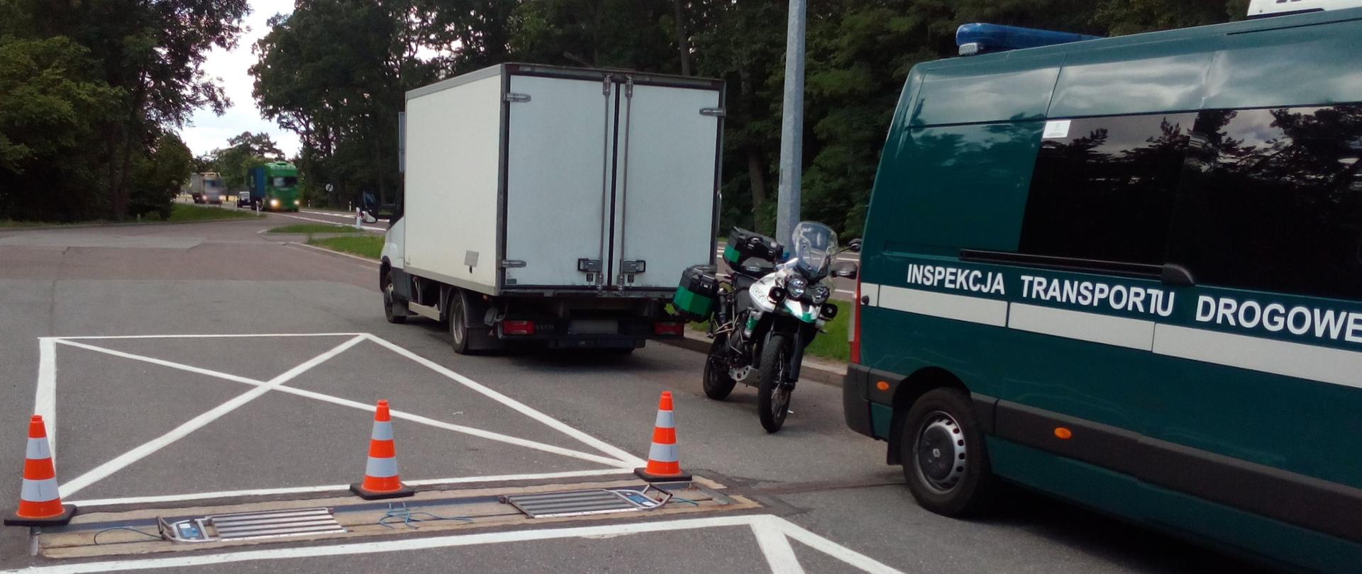Na pierwszym planie: przenośne wagi oraz stojący obok oznakowany furgon i motocykl ITD. W tle: zatrzymany do kontroli drogowej pojazd dostawczy. 