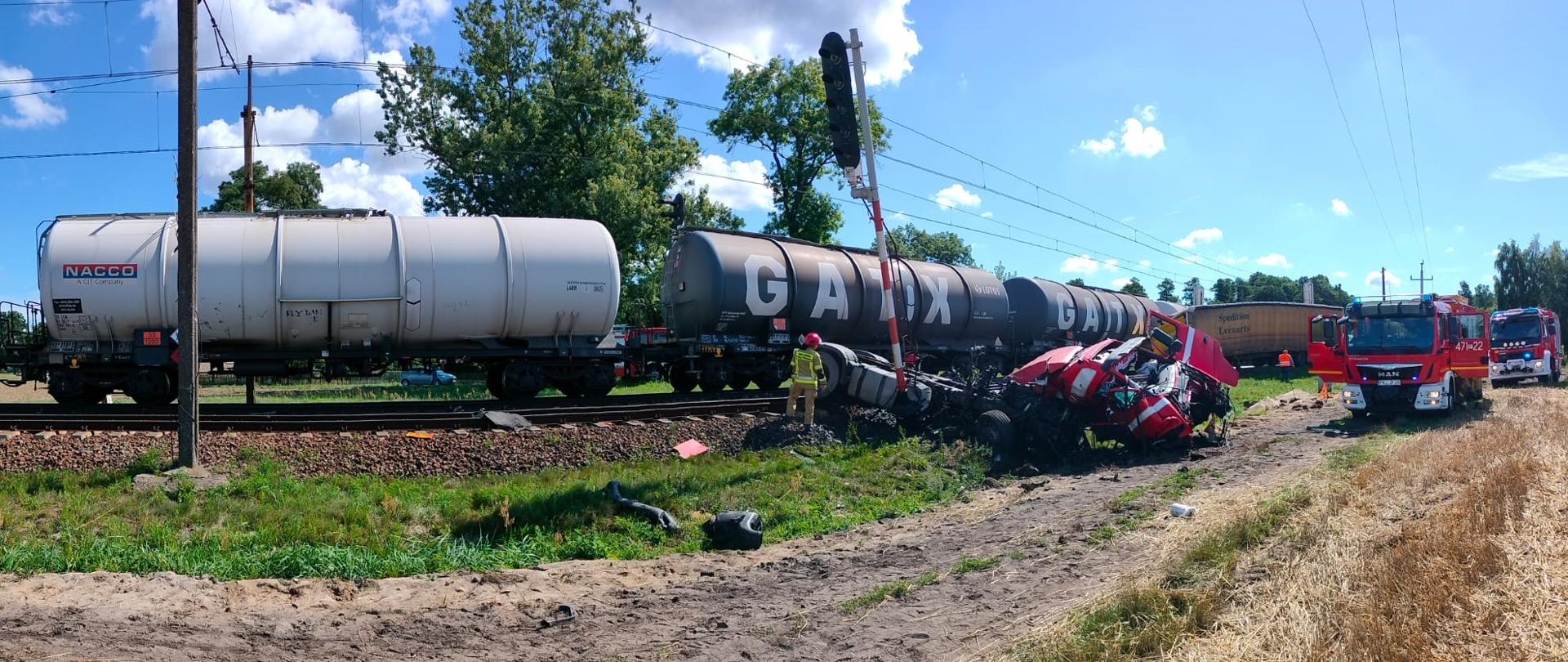 Zdjęcie przedstawia rozbity ciągnik siodłowy samochodu ciężarowego oraz wagony pociągu towarowego