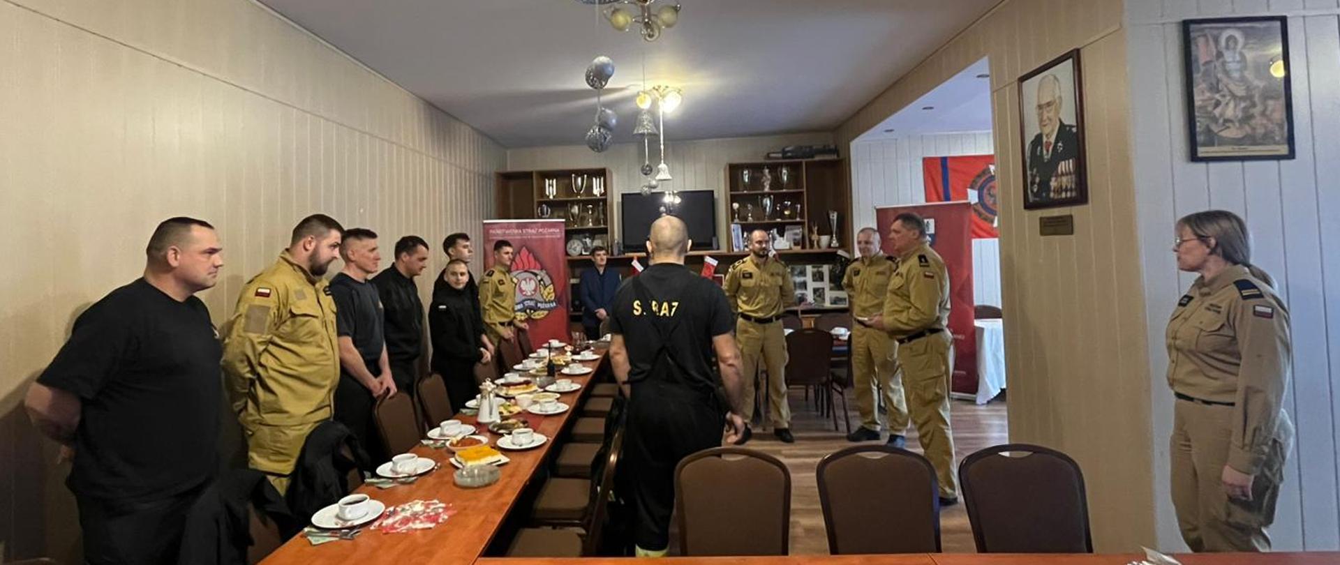 Funkcjonariusze Komendy Powiatowej Państwowej Straży Pożarnej w ubraniach koszarowych podczas spotkania opłatkowego z Komendantem Powiatowym brygadierem Marcinem Mazurkiewiczem