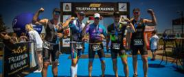 Pięć osób w strojach startowych frontem do obiektywu, w tle meta zawodów triathlonowych