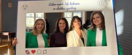 Na zdjęciu widać cztery kobiety pozujące za dużą ramką. Kobiety stoją obok siebie "wewnątrz ramki". Wszystkie są uśmiechnięte. Dwie skrajne kobiety (pierwsza od lewej i pierwsza od prawej) są ubrane w zielone marynarki. Druga kobieta od lewej ma na sobie ciemną koszulę, a trzecia od lewej jest ubrana w jasny, kremowy żakiet. Ramka jest duża, biała imitująca post z mediów społecznościowych. Na ramce znajdują się napisy: "#służbacywilna #WorkLifeBalance #RównowagaToSiła #Wellbeing. 