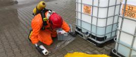 Strażak PSP z grupy chemicznej pracuje przy rozszczelnieniu mauzera na placu firmy