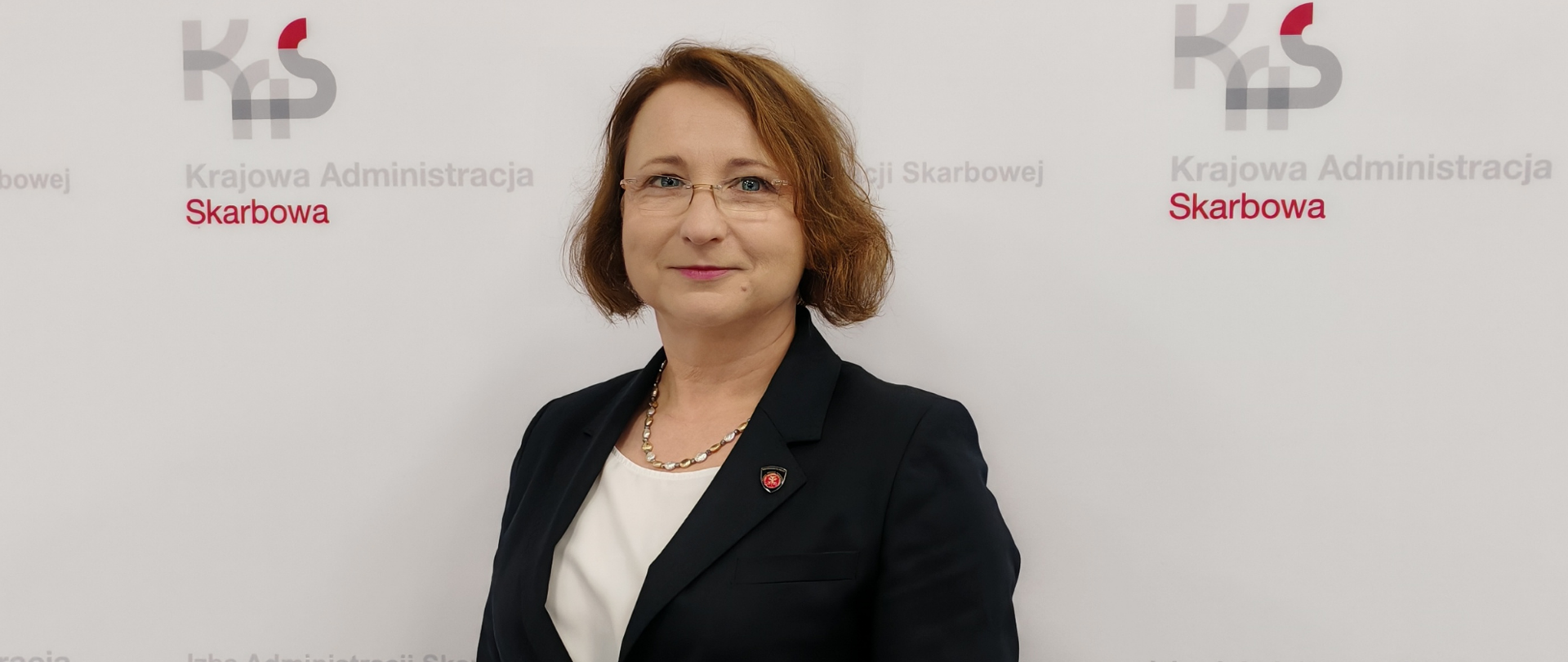 Kobieta na tle ściany z logo KAS i napisami Izba Administracji Skarbowej w Bydgoszczy