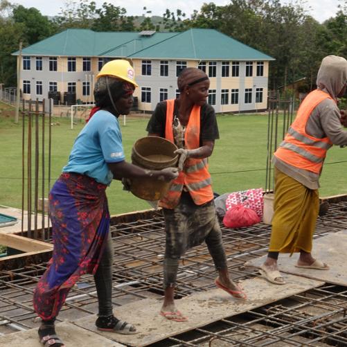 Kobiety pracujące przy budowie internatu podają sobie materiały budowlane.