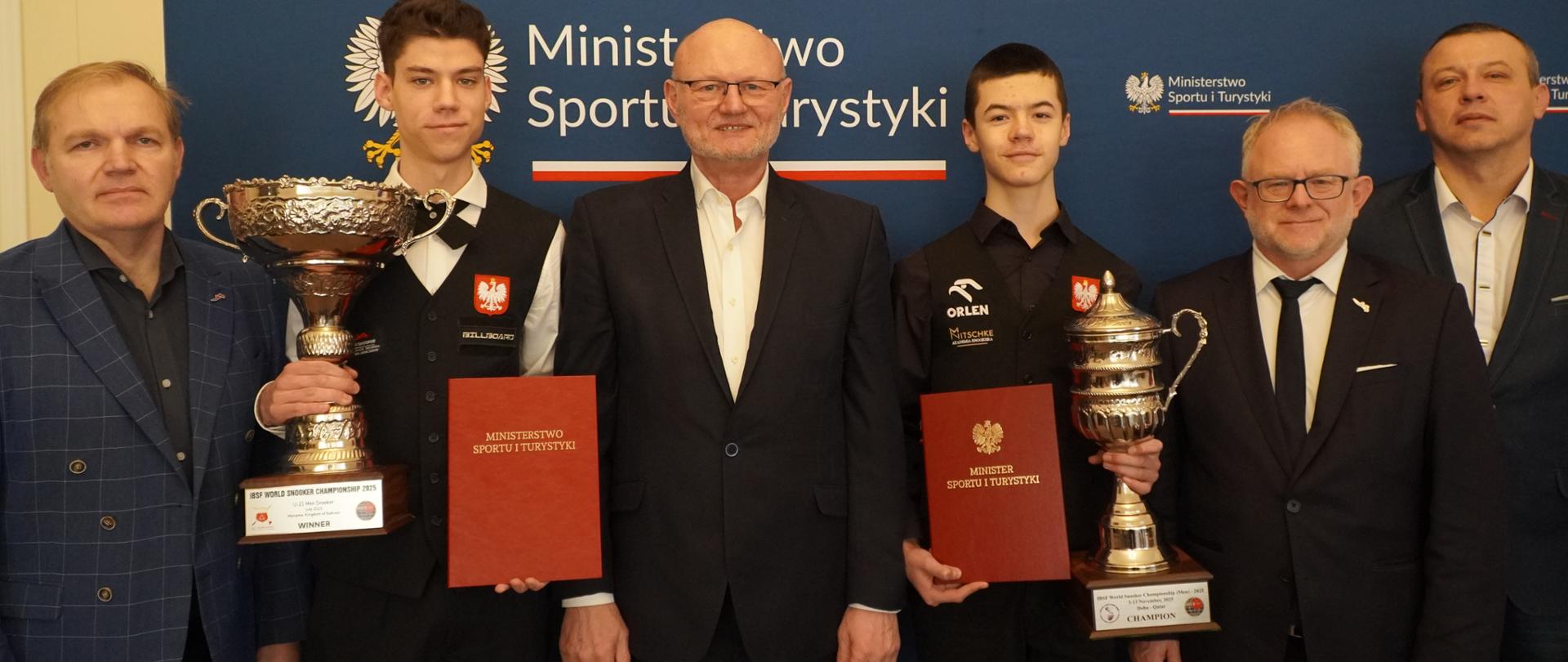 Zdjęcie zbiorowe na tle ścianki z logotypami Ministerstwa Sportu i Turystyki. Od lewej stroją: wiceprezes Polskiego Związku Snookera i Bilarda Angielskiego Piotr Murat, zawodnik snookera Sebastian Milewski (w rękach trzyma puchar i teczkę z napisem "Ministerstwo Sportu i Turystyki"), podsekretarz stanu w MSiT Ireneusz Nalazek, zawodnik snookera Michał Szubarczyk (w rękach trzyma puchar i teczkę z napisem "Ministerstwo Sportu i Turystyki"), prezes Polskiego Związku Snookera i Bilarda Angielskiego Romuald Lenkajtis, tata i trener Michała Szubarczyka - Kamil Szubarczyk.