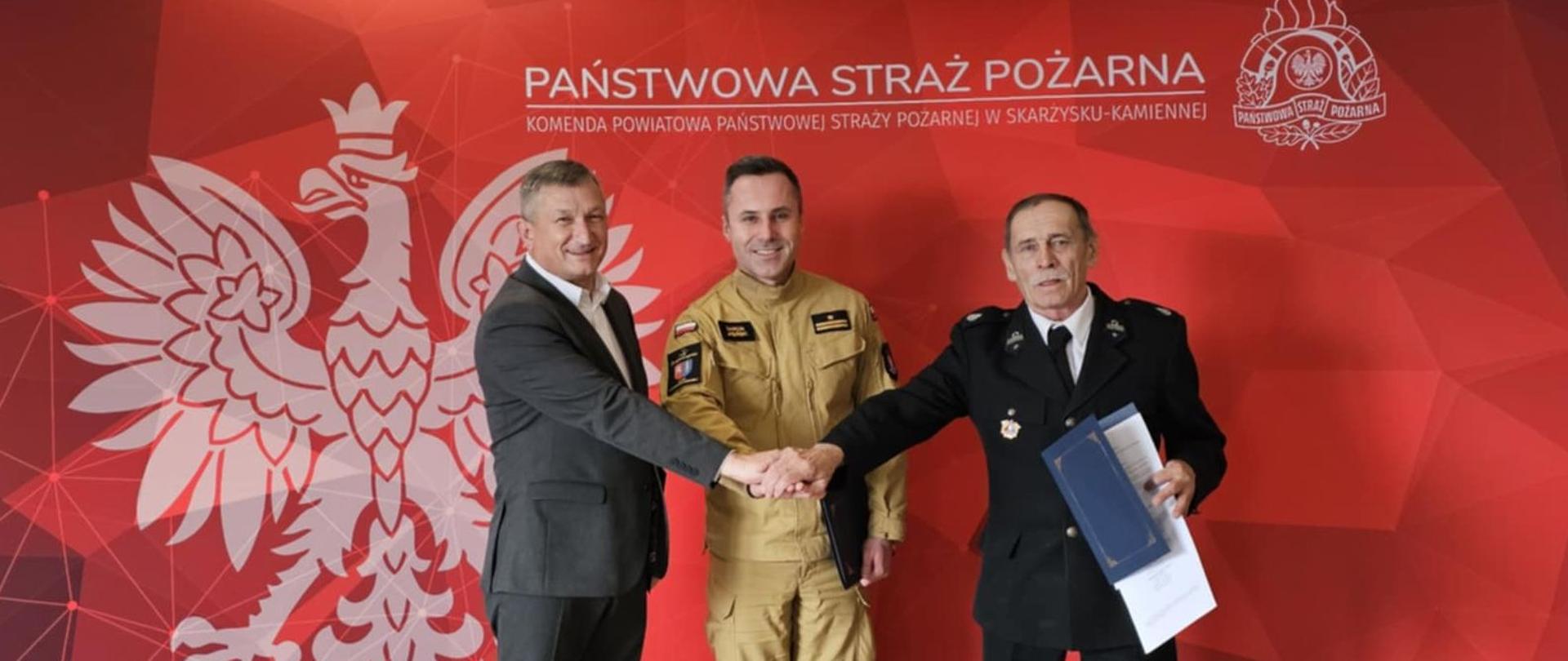 Na zdjęciu widać Burmistrza Miasta i Gminy w Suchedniowie, który wraz z Komendantem Powiatowym PSP w Skarżysku-Kamiennej gratulują Prezesowi OSP Ostojów włączenia jednostki do Krajowego Sytemu Ratowniczo Gaśniczego.