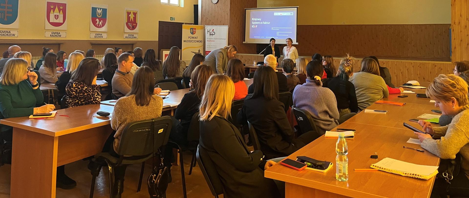Przy stołach siedzi grupa osób i słucha wykładu o usłudze KSeF