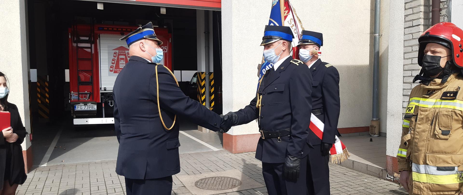 Zdjęcie przedstawia Komendanta Powiatowego Państwowej Straży Pożarnej w Krośnie Odrzańskim gratulującemu funkcjonariuszowi otrzymania wyższego stopnia służbowego. 