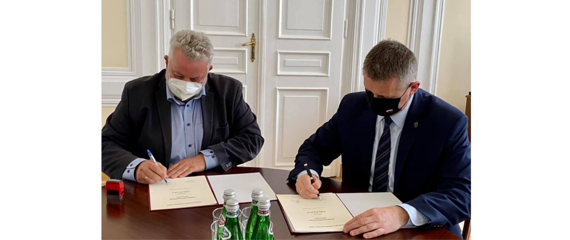 Na zdjęciu znajduje się dwóch mężczyzn podpisujących umowy