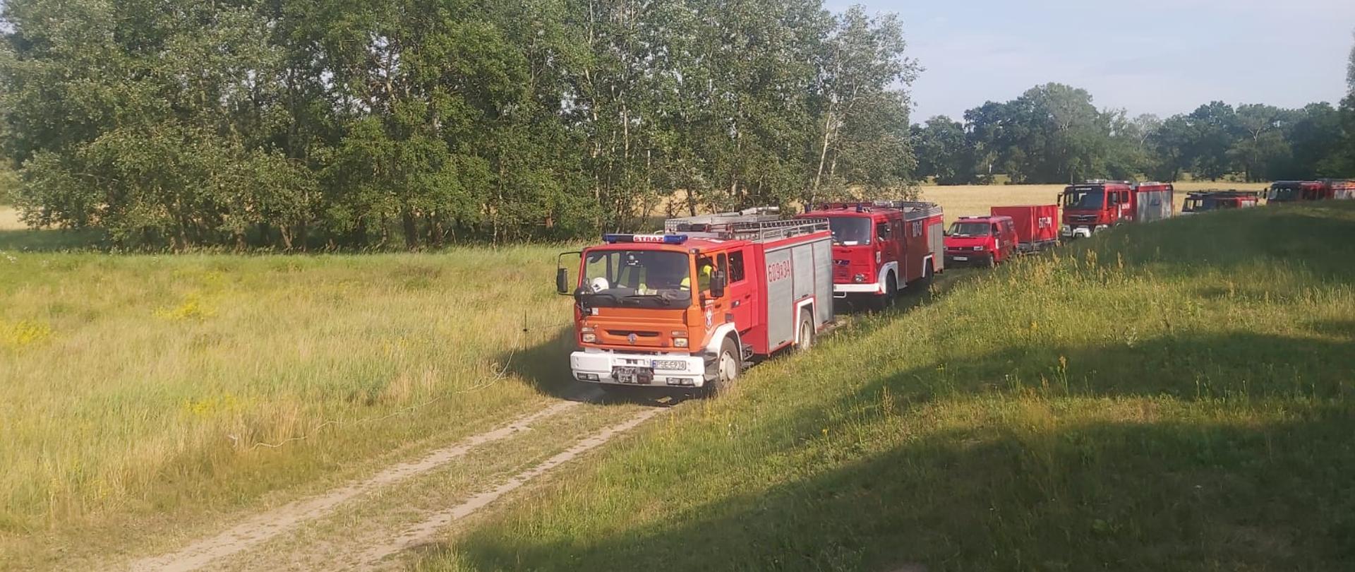 Na drodze przy wale przeciwpowodziowym jedzie kolumna samochodów ratowniczo - gaśniczych i specjalnych