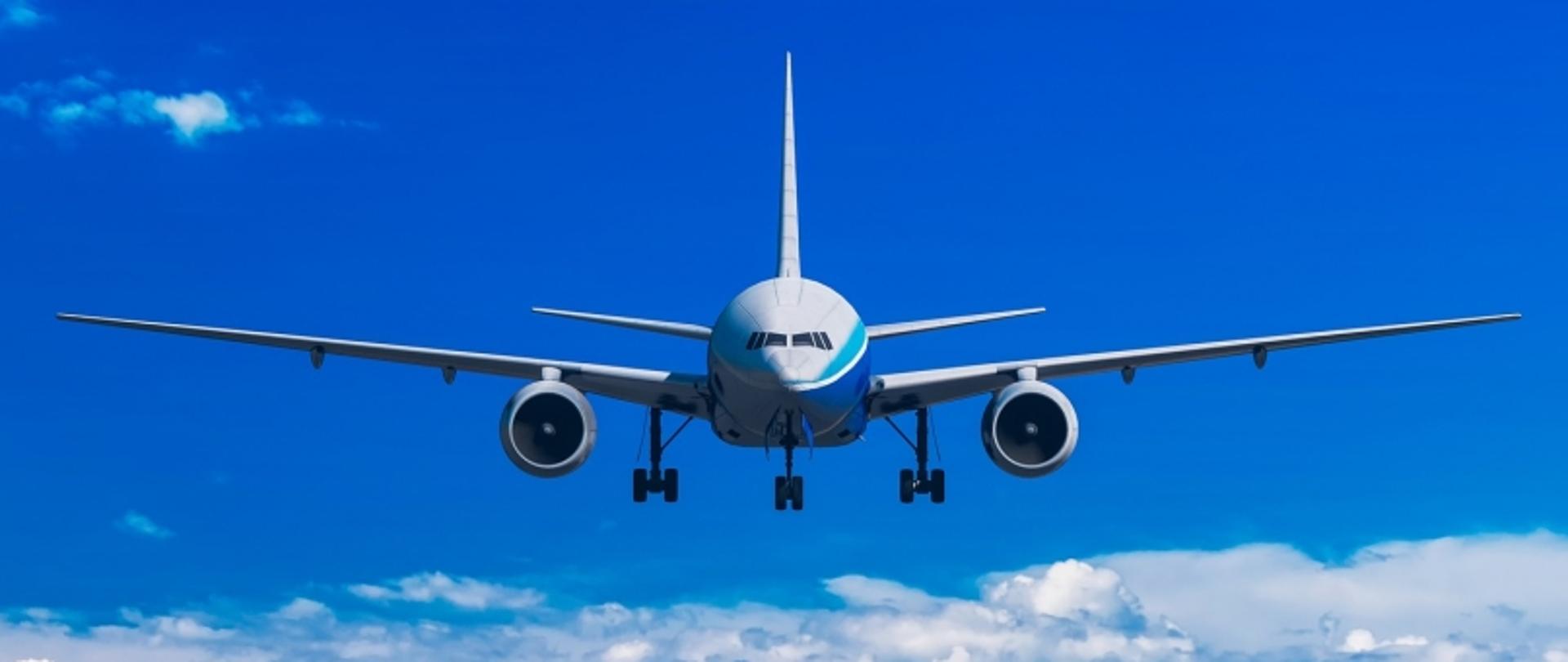 Samolot pasażerski w locie na tle nieba, widok z przodu, widoczne skrzydła i silniki.