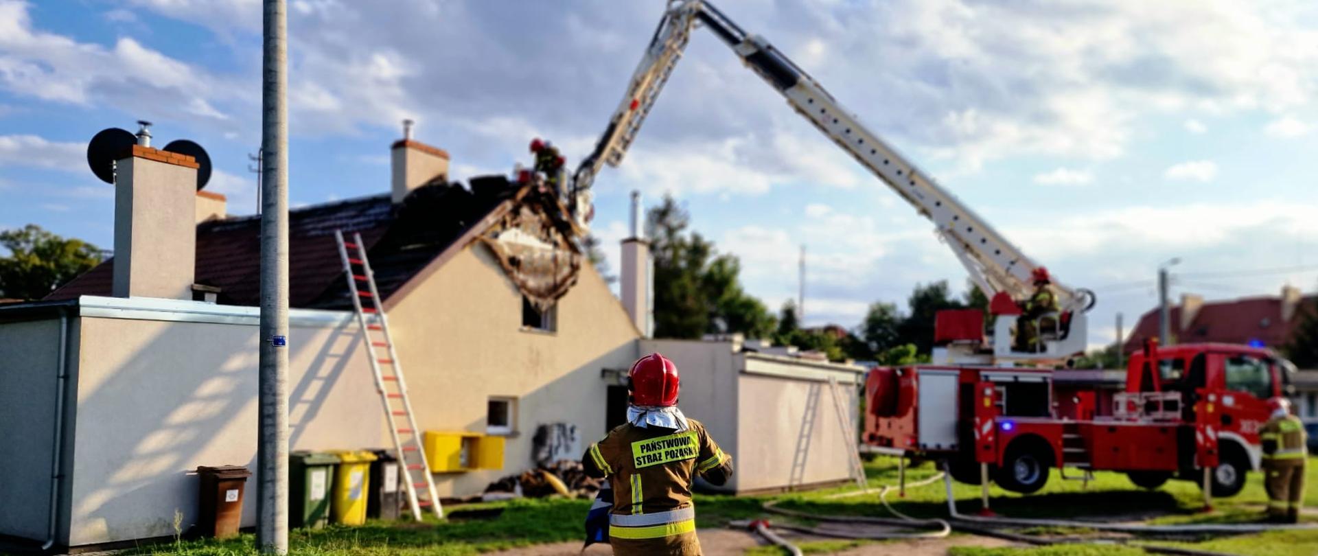 Zdjęcie przedstawia dowódcę akcji gaśniczej oraz strażaków gaszących pożar z wykorzystaniem podnośnika.