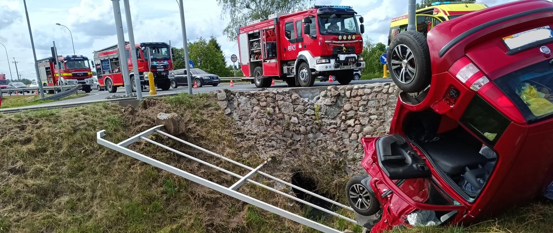 Zdjęcie przedstawia samochód marki Fiat na leżący na dachu w rowie