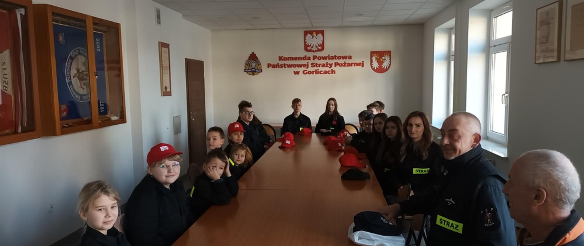 Na zajęciu na sali konferencyjnej Komendy Powiatowej Państwowej Straży Pożarnej w Gorlicach dzieci z młodzieżowej drużyny pożarniczej z Ochotniczej Straży Pożarnej z Biesnej podczas słuchają prelekcji na temat ochrony przeciwpożarowej w ramach akcji Podsumowanie akcji bezpieczne zimowisko-otwarte strażnice 2023 