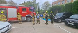 Na zdjęciu widzimy strażacki samochód gaśniczy oraz kilku strażaków podczas ćwiczeń.