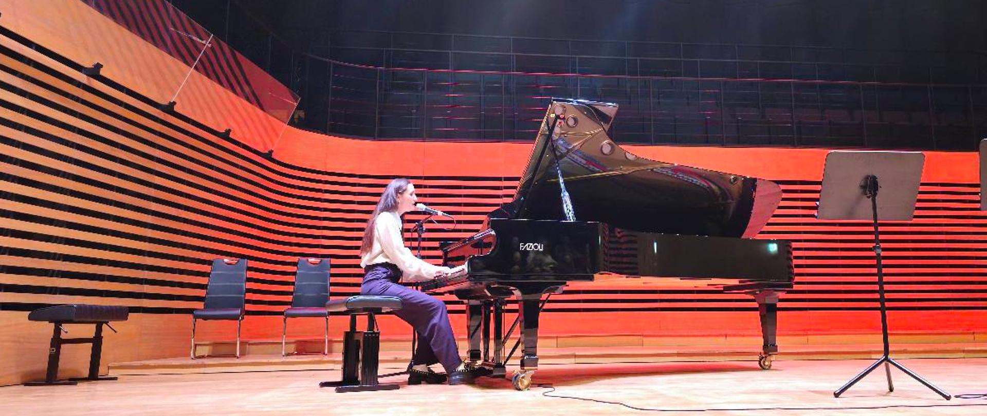 Kobieta gra na fortepianie i śpiewa.