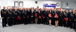 Druhowie ochotniczych straży pożarnych oraz zaproszeni goście stoją wspólnie razem.