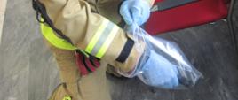 Strażak pobiera materiał chemiczny do woreczka strunowego w ubraniu specjalnym i aparacie ochrony dróg oddechowych.