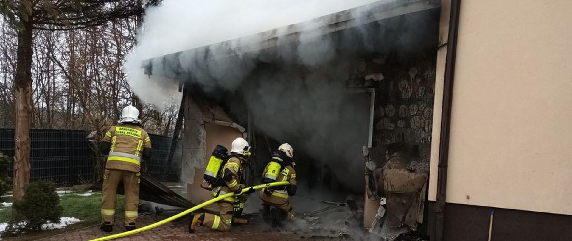 Strażacy podają wodę na garaż z którego wydobywa się dym