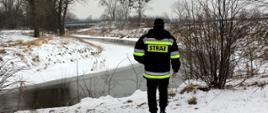 Na zdjęciu jest Strażak, który idzie wzdłuż linii brzegowej rzeki, kontrolując poziom wody w korycie rzeki.