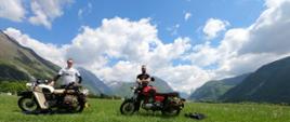 Na zdjęciu dwóch motocyklistów wraz z motocyklami. W tle krajobraz.
