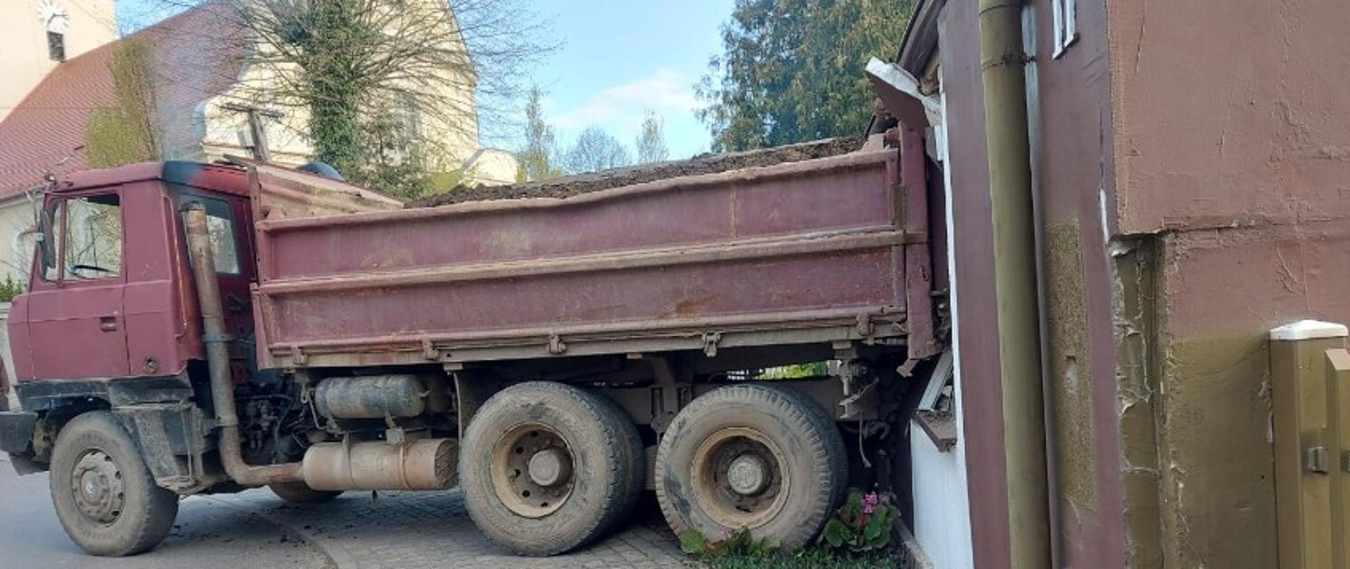 Widać samochód ciężarowy od strony kierowcy, który tyłem uderzył w budynek