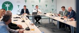 Ogólny widok sali konferencyjnej podczas spotkania przedstawicieli Inspekcji Transportu Drogowego i organizacji zrzeszających przewoźników drogowych. Główny Inspektor Transportu Drogowego Robert Koźlak zabiera głos podczas spotkania. W tle widoczne są elementy identyfikacji wizualnej Inspekcji Transportu Drogowego.