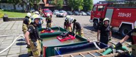Strażacy ochotniczych straży pożarnych przy punkcie czerpania wody na tle rynku w Lanckoronie
