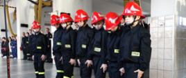 MDP w ubraniach koszarowych koloru czarnego i czerwonych hełmach stoją w garażu w szeregu.